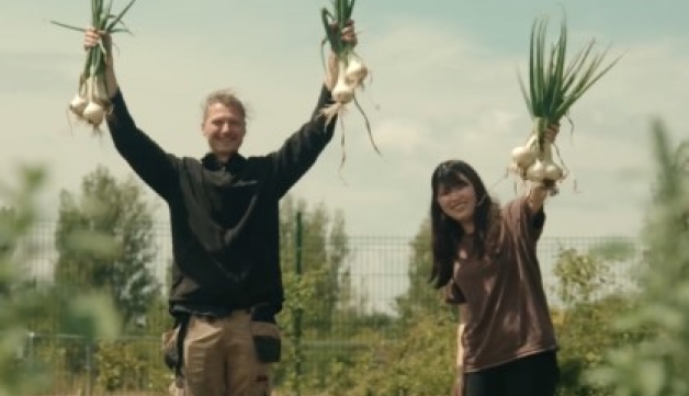 Two people hold aloft onions in a community allotment.