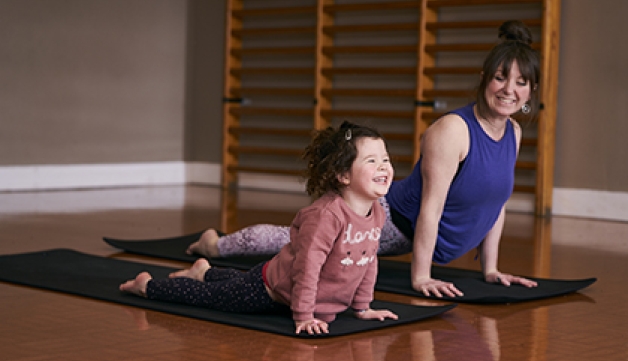 A smiling mother and daughter practice yoga together, side by side