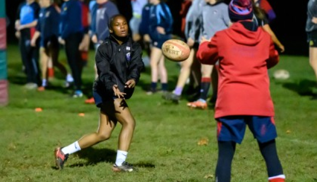 A girl passes a rugby ball to a coach during a training session.