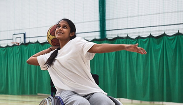 A South Asian young female shoots at the basket while playing wheelchair basketball in a sports hall