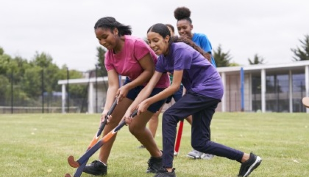 Two girls contest the ball during a game of hockey on a grass pitch.