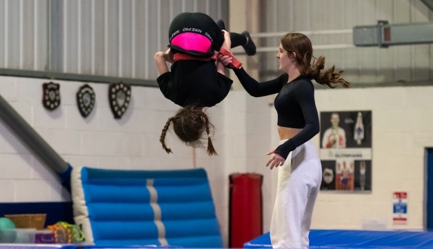 A female coach helps a young girl tumble in a gymnastics and trampolining hall.
