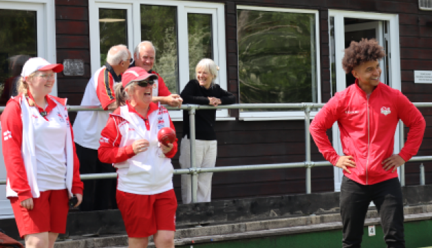 A group of bowlers wearing Team England kit laugh together on a green.