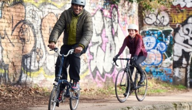 Couple wearing helmets cycle down the side of a canal in line