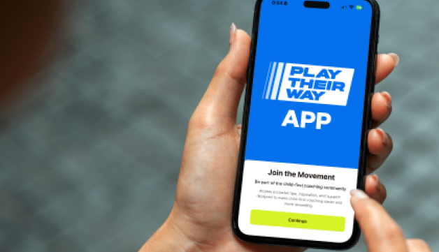 A hand holding a phone on which the Play Their Way app is displayed