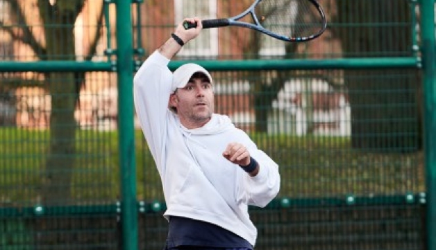 A male tennis player hits a forehand shot on an outdoor court.