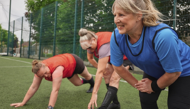 A group of women perform stretches on an artificial grass pitch, ahead of a walking football match