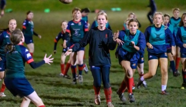 A group of girls play rugby on a field at night.