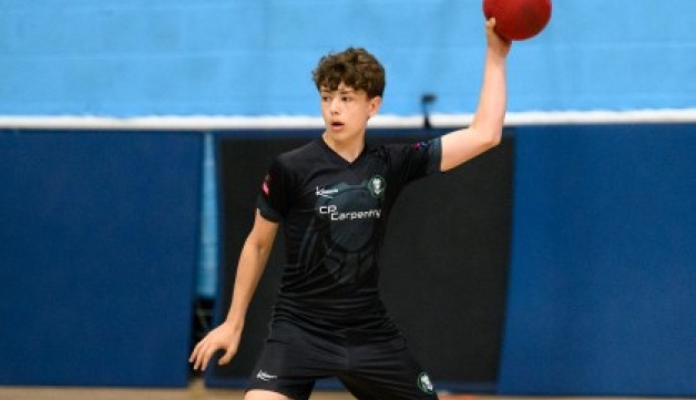 A boy prepares to throw a dodgeball in a school hall.