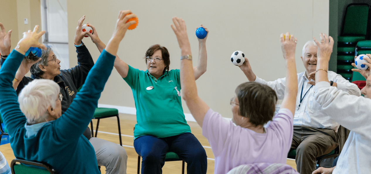 A class takes part in sitting exercises with mini footballs