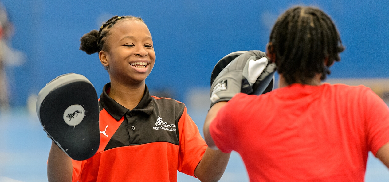 Two schoolgirls boxing inside a sports hall.