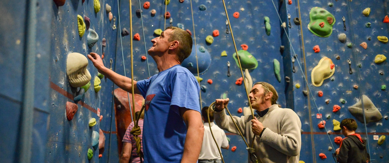 A man looks up a climbing wall as he and others prepare to climb it.