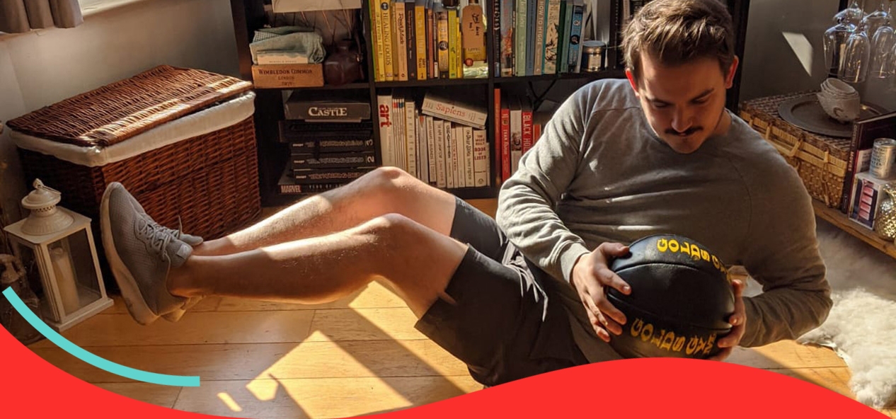 A man performs Russian twists using a medicine ball in his own living room