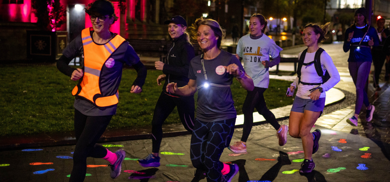 Women running over glow-in-the-dark footprints in a city at night