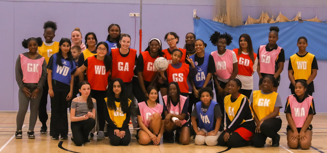 Girls  in their Netball Bibs take a group picture in sport hall