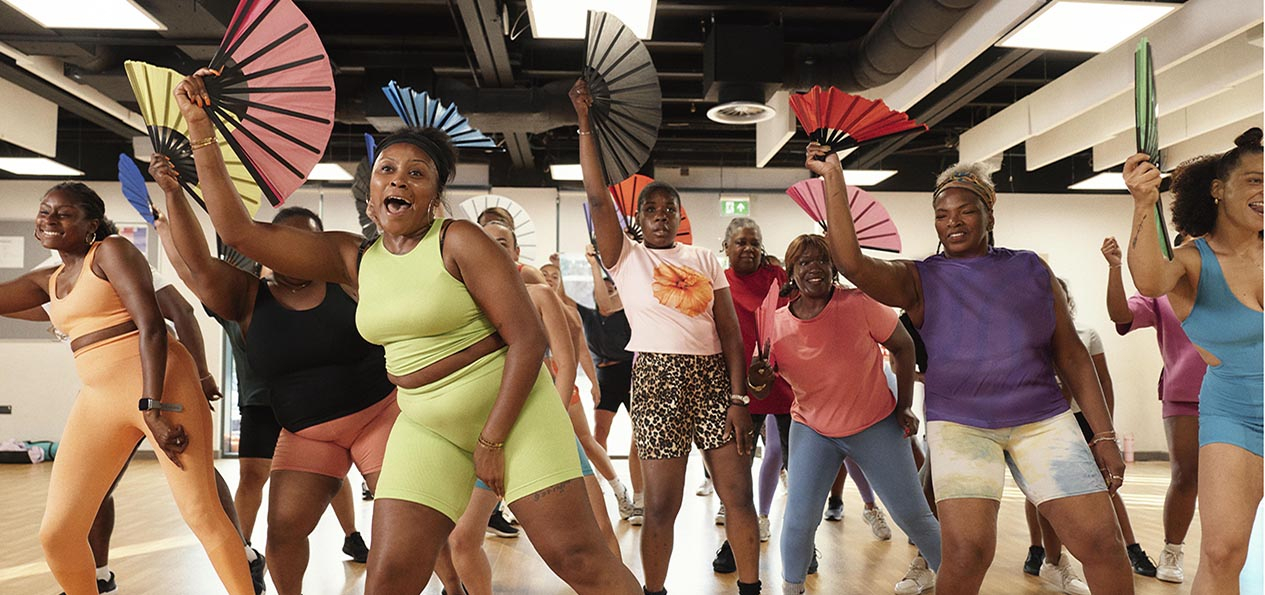 A group of women perform a dance routine in a class, holding and waving paper fans