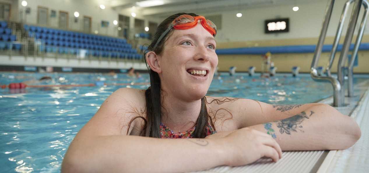 A female swimmer smiles as she leans on the side of the pool.