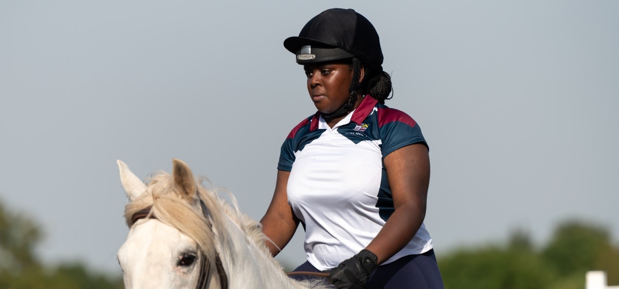 A young Black woman rides a horse during an equestrian event.