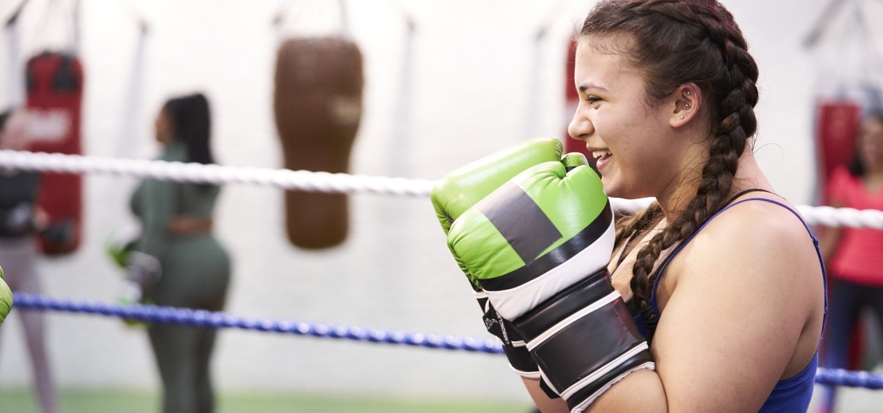 A girl wearing boxing gloves smiles as she stands in a defensive guard in the ring