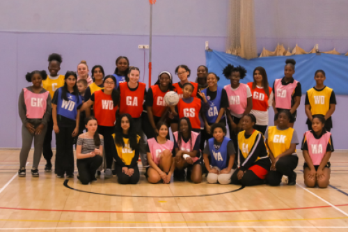 Girls  in their Netball Bibs take a group picture in sport hall