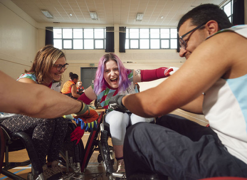 Three wheelchair rugby players arrange themselves in a circle and put their hands together to prepare for a match