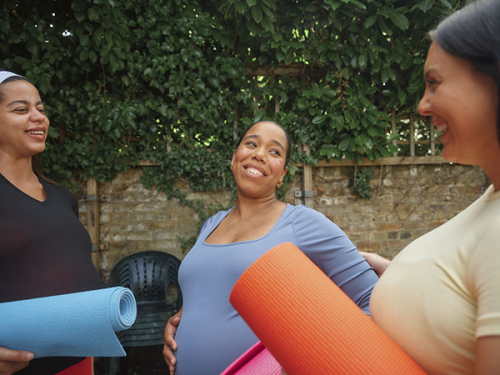 Three pregnant women smile while holding yoga mats