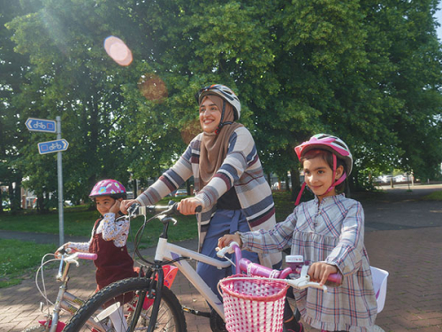 A woman and her two daughters all ride their bikes in a park