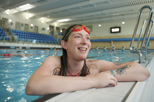 A pregnant woman wearing goggles leans on the edge of a swimming pool