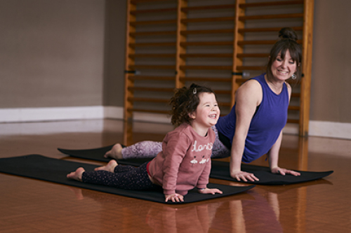 A smiling mother and daughter practice yoga together, side by side