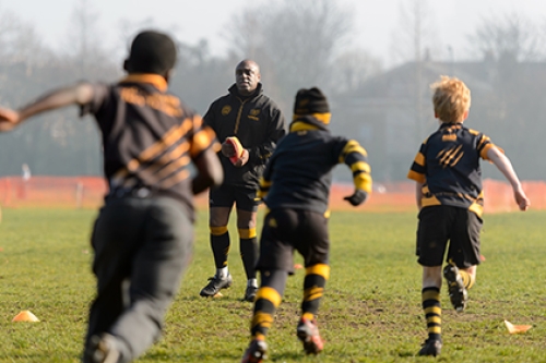  A group of boys run towards their coach during an outdooors rugby training session on a sunny day.
