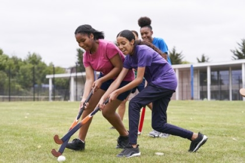 Two girls contest the ball during a game of hockey on a grass pitch.