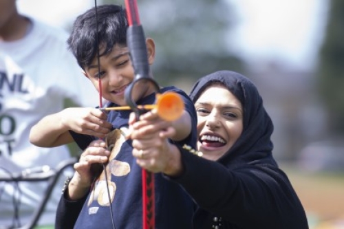 A crouching mum helps her son hold his bow and arrow while he aims during an archery session.