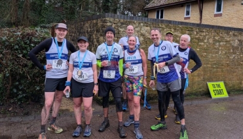 A group of runners from Chippenham Harriers pose for a photo in front of a wall, with medals around their necks.