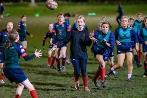 A group of girls play rugby on a field at night.