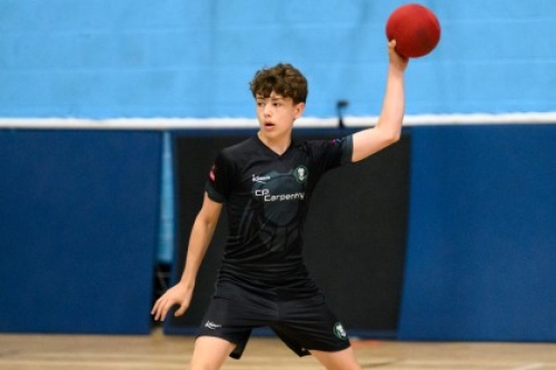A boy prepares to throw a dodgeball in a school hall.