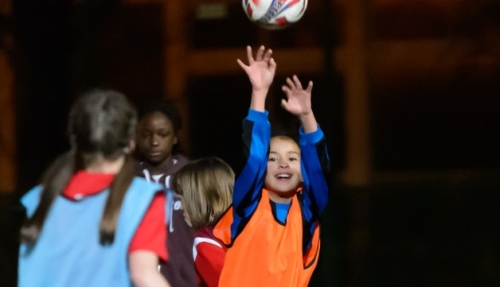 A smiling girl throws a football during a training session at night.