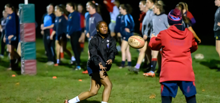 A girl passes a rugby ball to a coach during a training session.