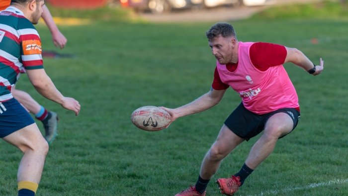 A rugby player holding the ball looks to evade an opposing player's tackle.