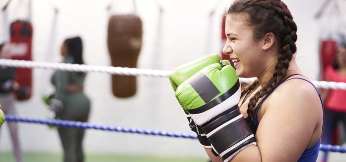 A girl wearing boxing gloves smiles as she stands in a defensive guard in the ring