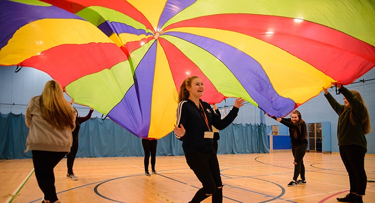 A group of girls holding a colourful sheet above their heads in a sports hall.