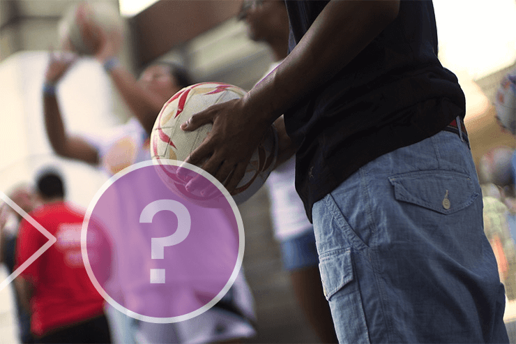 A person holding a basketball, while someone takes a shot behind.