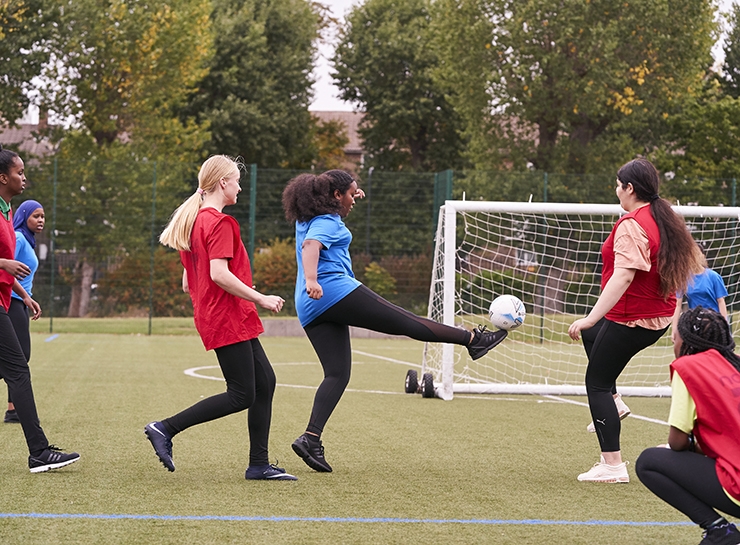 A woman kicks the ball towards goal during an outdoor game of football.