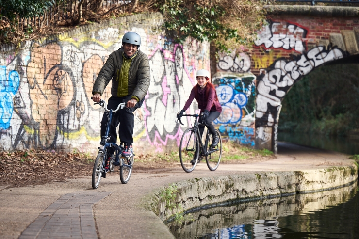 Couple wearing helmets cycle down the side of a canal in line 