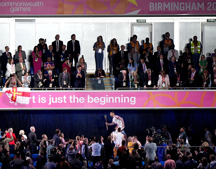 Max Whitlock carries the Queen's Baton at the Opening Ceremony of the Birmingham 2022 Commonwealth Games, in front of a sign reading 'sport is just the beginning'
