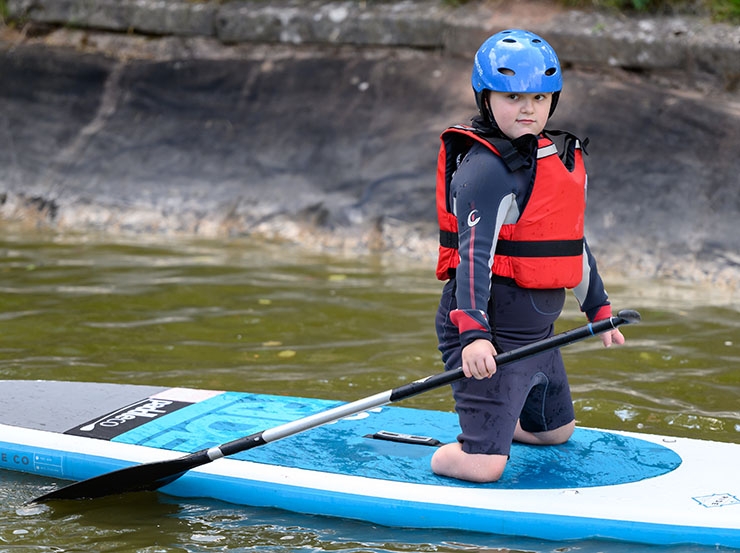 A double amputee-of-the-legs boy, kneels on a paddle board