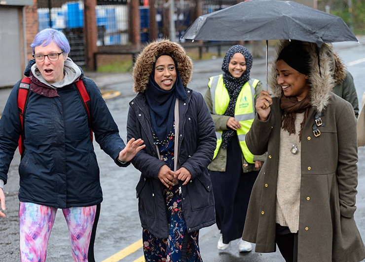People smiling while walking down a street, with one person holding an umbrella