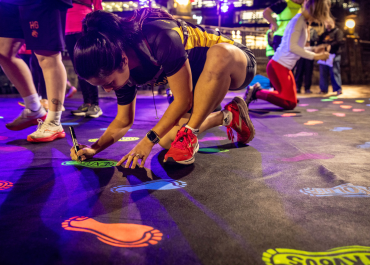 A runner writes on a glow-in-the-dark footprint sticker on the ground