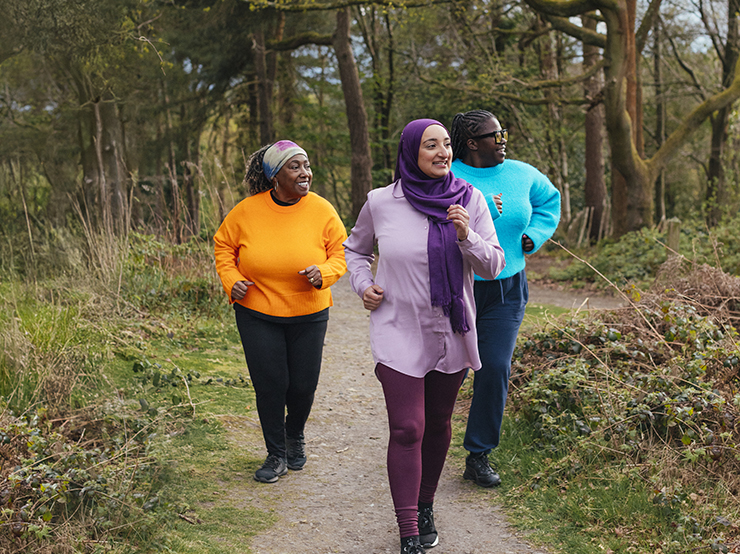 Three women running on a path through a wooded area