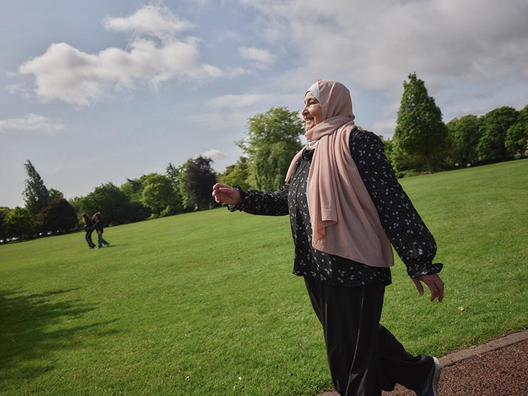 A pregnant woman wearing a headscarf walks in a park