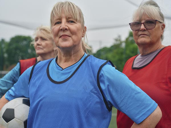 Three female walking football players pose for a photo, with hands on their hips and one of them holding the ball under their arm